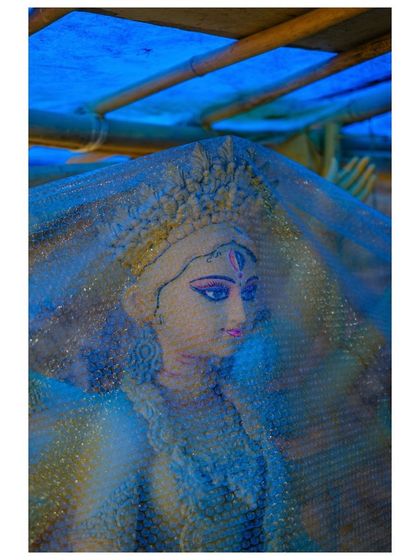 A finished idol of a goddess is covered with bubble wrap for transport, her serene face visible through the protective layer.