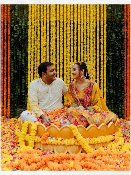 The couple sits in a lotus-shaped vessel surrounded by a sea of marigolds during their Haldi ceremony. This photo highlights the beautiful decor and happy moments of the ritual.