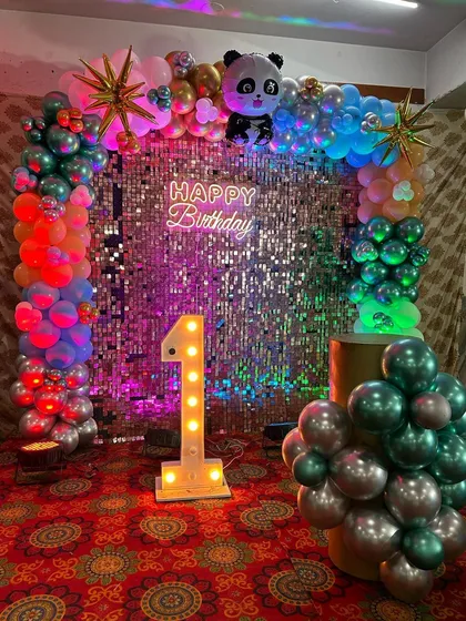 A vibrant first birthday party with a multi-colored balloon arch, panda and Captain America accents, and a shimmer backdrop.