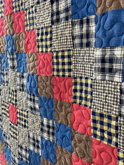 A close-up of a memory quilt made from plaid and checked shirts, finished with a gentle, curving quilting pattern.