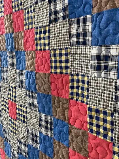 A close-up of a memory quilt made from plaid and checked shirts, finished with a gentle, curving quilting pattern.