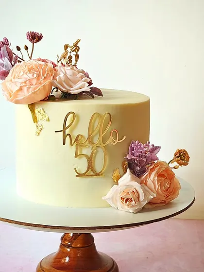 "Hello 50." A sophisticated cake for a 50th birthday, decorated with beautiful fresh flowers and a stylish gold topper. The simple elegance of this design makes it a timeless choice.