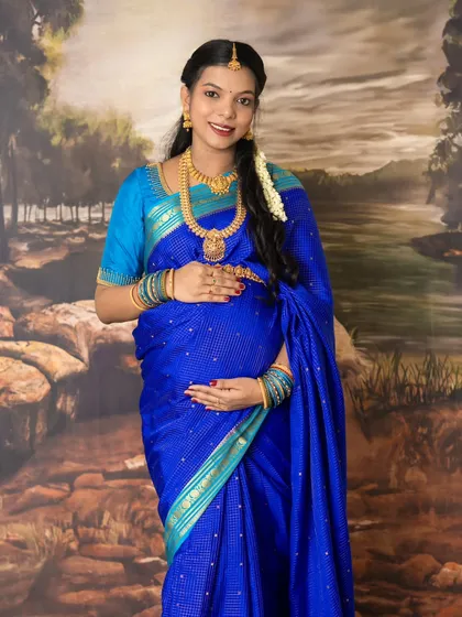 Embracing tradition and elegance. This studio maternity photo captures the timeless beauty of a mother-to-be in a stunning blue silk saree, adorned with traditional jewelry and flowers.