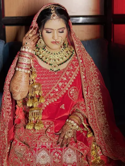 A regal bridal portrait. The bride is wearing a magnificent red velvet lehenga with heavy jewelry, and the makeup is designed to be equally grand, with bold eyes and a perfectly sculpted face.