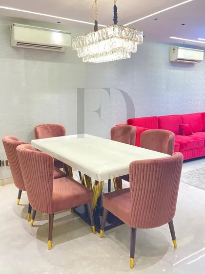 This dining set is perfect for a modern home, featuring a white onyx table with a sculptural gold base. The chairs, upholstered in a pleated rose-colored velvet, add a pop of color and texture.