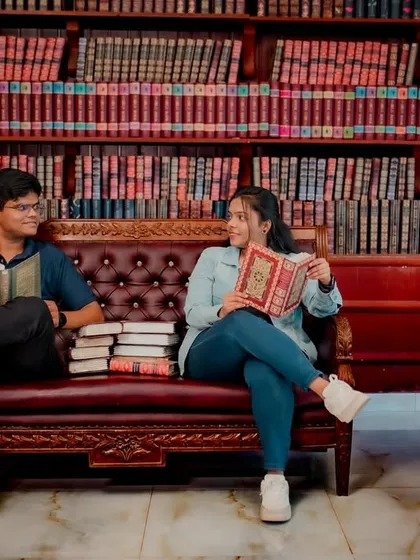 Another shot from the library-themed shoot. The couple sits on a classic leather couch, sharing a look while holding books, perfectly capturing their shared interest.