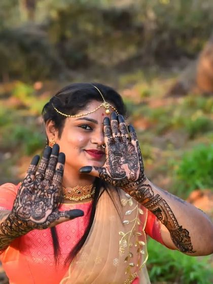 A stunning outdoor shot of a bride, her face peeking through her beautifully hennaed hands. The dark stain looks incredible in the natural light.