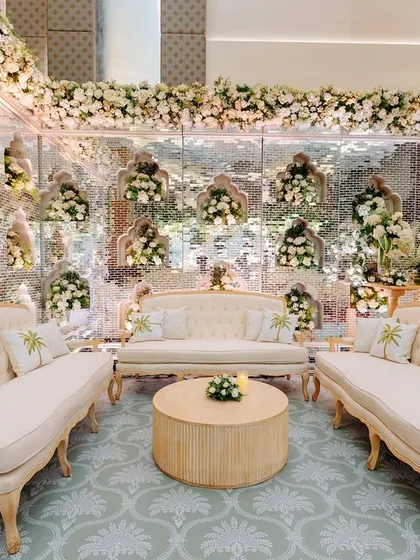 An opulent lounge setting where classic French-style sofas are placed against a wall of mirrors, reflecting the lush white floral decor. This design creates a sense of infinite space and timeless elegance.