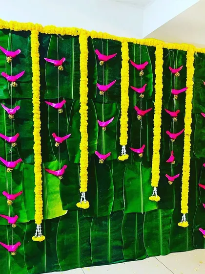 An eco-friendly and charming backdrop created with fresh banana leaves, vertical marigold garlands, and decorative bird hangings. This natural theme is a wonderful choice for daytime functions and traditional ceremonies like a baby shower or Haldi.