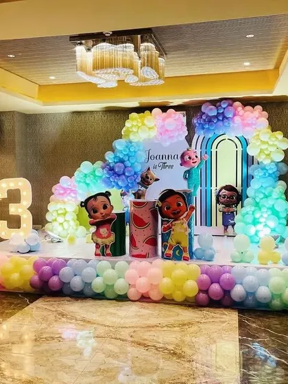 A large stage setup for a Cocomelon-themed 3rd birthday, using pastel rainbow balloons and multiple character props.
