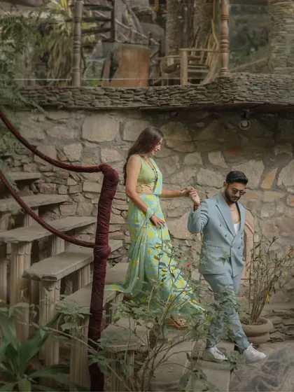 Descending a winding stone staircase, the couple is captured in a moment of quiet connection. The natural, earthy tones of the location complement their vibrant and modern attire.