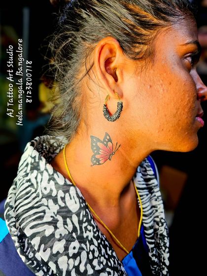 A small, colorful butterfly tattoo on the neck, a delicate and beautiful placement.
