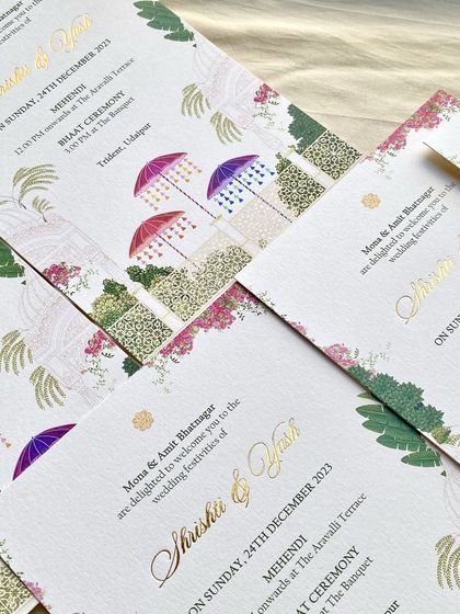 A pattern of Mehendi and Bhaat ceremony cards for the Udaipur wedding. The design combines colorful umbrellas, bougainvillea, and palm illustrations with elegant gold foil script.