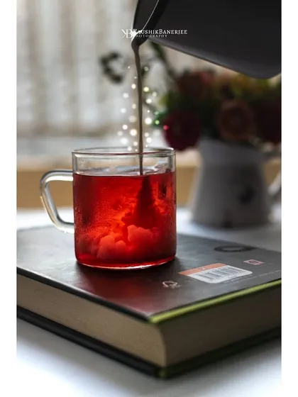 An action shot of a tea concentrate being poured into a glass mug. The backlighting illuminates the red liquid, creating a beautiful visual of the tea-making process.