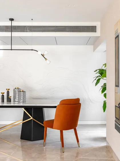 A detail from the Evelyn duplex, this view highlights the flow between spaces. The bold orange dining chair adds a pop of color against a custom wall with subtle, wave-like textures, creating a sense of movement and artistry that connects the dining and living areas.