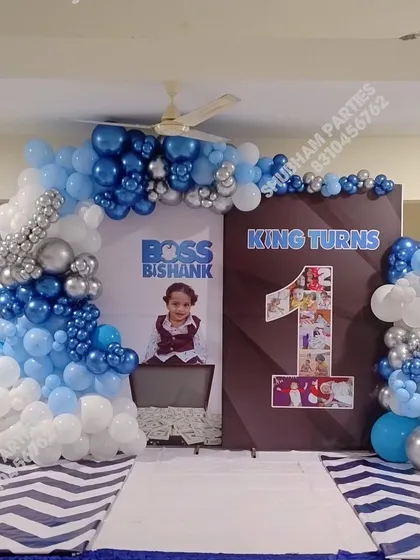 A "Boss Baby" themed first birthday party with a custom backdrop and a blue, white, and silver balloon arch.