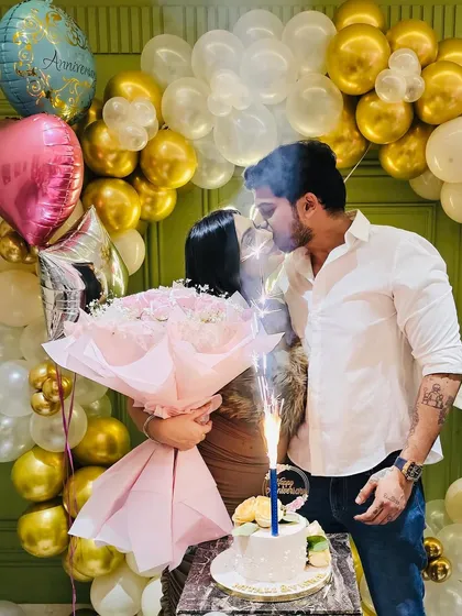 A romantic moment captured during an anniversary celebration. The warm glow of the neon sign and the festive balloons create a beautiful atmosphere.