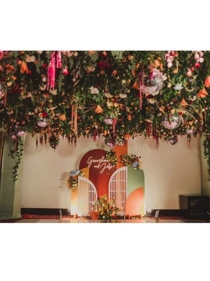 The full stage setup for the fall-themed reception. The backdrop features modern arched panels in earthy tones, complementing the vibrant floral installation above.