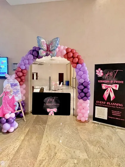 The party entrance, featuring a balloon arch in shades of purple and pink, topped with a large butterfly balloon. My company banner and a welcome sign greet the guests.