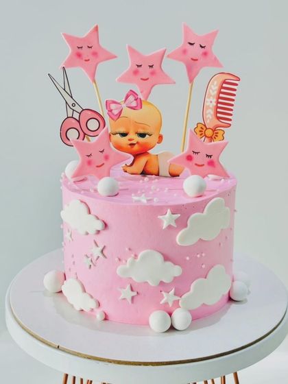 A sweet cake for a baby's naming ceremony. The pink cake is decorated with clouds, stars, and cute toppers like a comb and scissors.