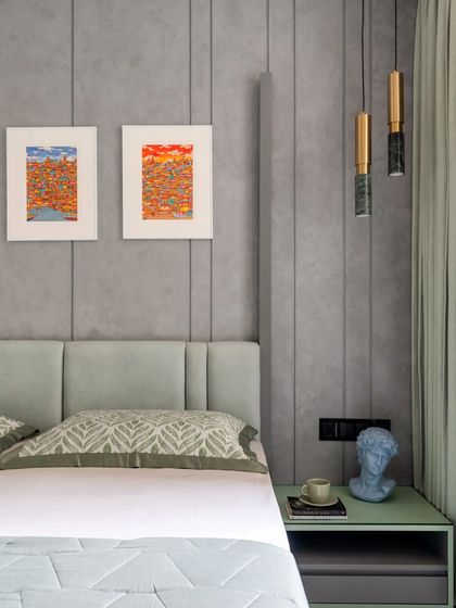 This contemporary bedroom uses a cool, neutral palette to create a calming environment. The paneled grey wall adds subtle texture, while pops of color from the artwork and the mint green bedside table bring a touch of personality. Marble and brass pendant lights add a final touch of elegance.