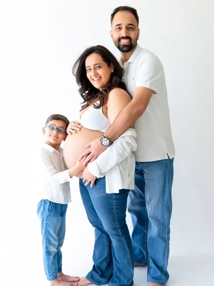 A heartwarming family maternity photo where an older sibling joins his parents to embrace the baby bump. This shot captures the excitement of the entire family in a clean, modern studio style.