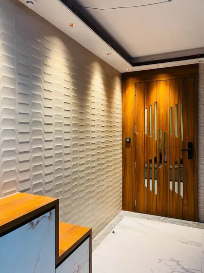 An elegant entrance featuring a wooden door with diagonal glass inserts and a textured 3D wall panel. The spotlights from above highlight the textures of both the wall and the door.