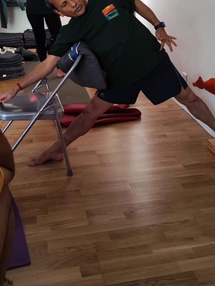 Teaching a student how to use the wall and a chair for a supported triangle pose. This setup helps in understanding the rotation of the torso and grounding of the feet.