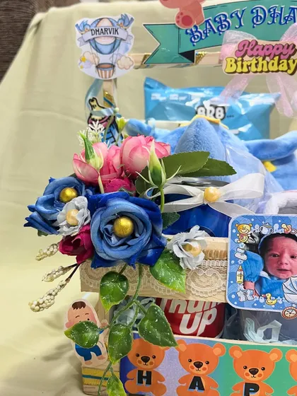 A side view of the baby milestone hamper, showing the arrangement of blue and pink flowers alongside a framed photo of the baby. It’s a beautiful blend of fresh elements and personal keepsakes.