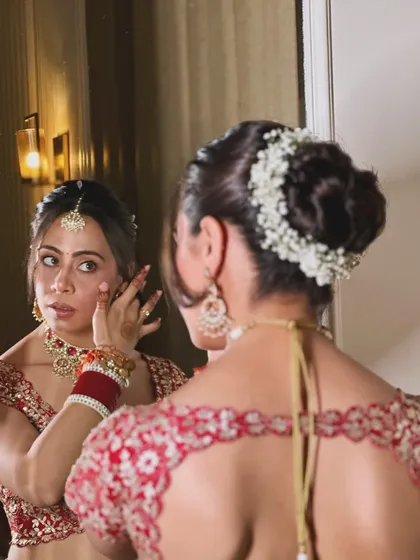 Simplicity, elegance, and grace. A beautiful shot of the bride looking in the mirror, with a classic red lehenga and a simple, elegant floral bun.