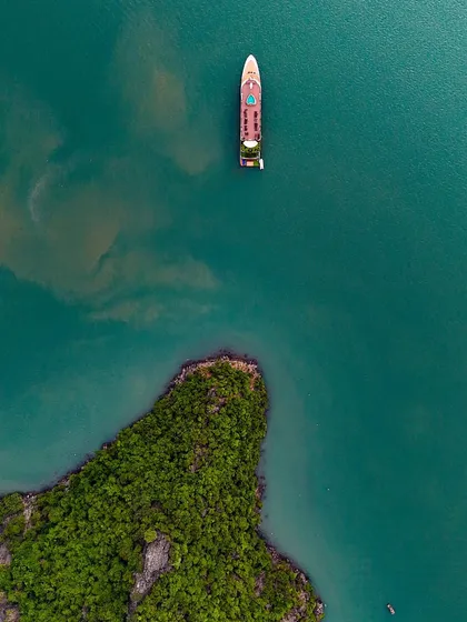A lone ship sails near an island in Ha Long Bay. The top-down perspective emphasizes the solitude and vastness of the sea.