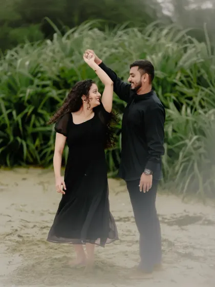 A couple in matching black outfits shares a dance on the beach, a simple and elegant pre-wedding shot.