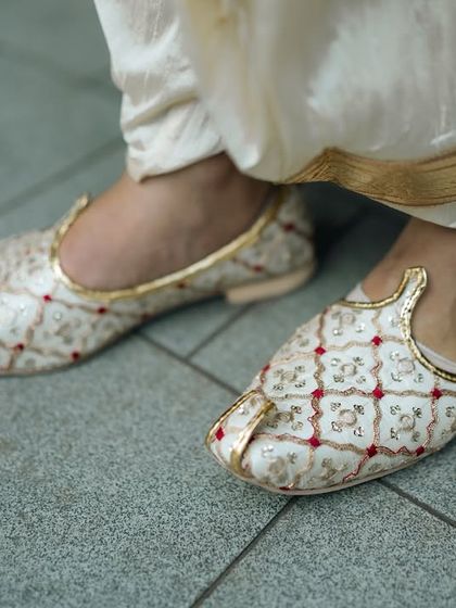 A detail shot of the groom's traditional wedding shoes, or juttis, adding to his overall ethnic look.