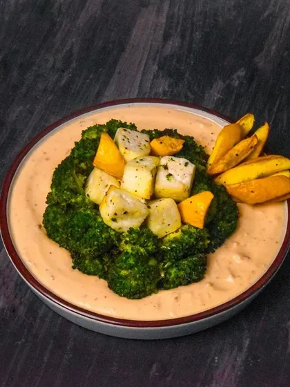 A creative dish of steamed broccoli and paneer in a creamy sauce, with a side of potato wedges. The dark, minimalist styling gives it an artistic and gourmet feel.