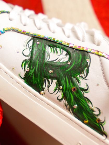 A macro shot of the custom initial on the Rare Rabbit sneakers. You can see the detailed brushstrokes in the green "R" and the carefully placed crystals that outline the panel.