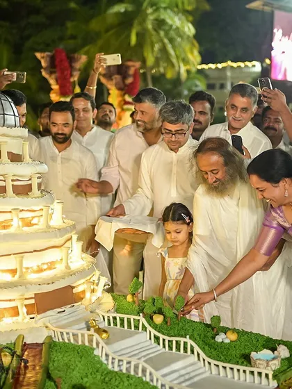 A moment of pure joy during Gurudev Sri Sri Ravi Shankar's birthday celebration. The centerpiece is a magnificent cake shaped like the Vishalakshi Mantap, shared by the entire community.