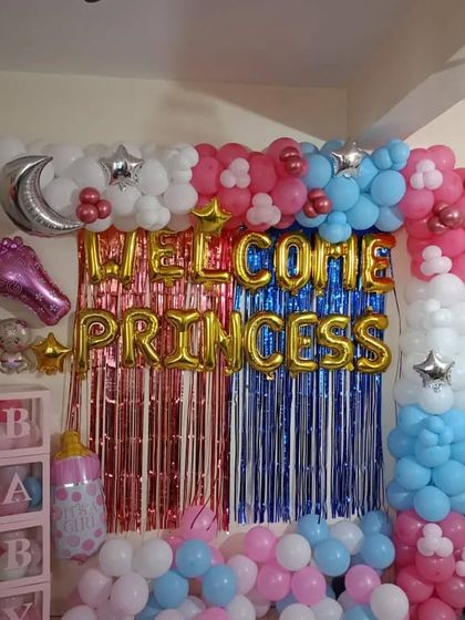 A vibrant "Welcome Princess" decoration using a split-color foil curtain in pink and blue. The setup is framed by a balloon garland and includes a silver moon foil balloon and "BABY" blocks.