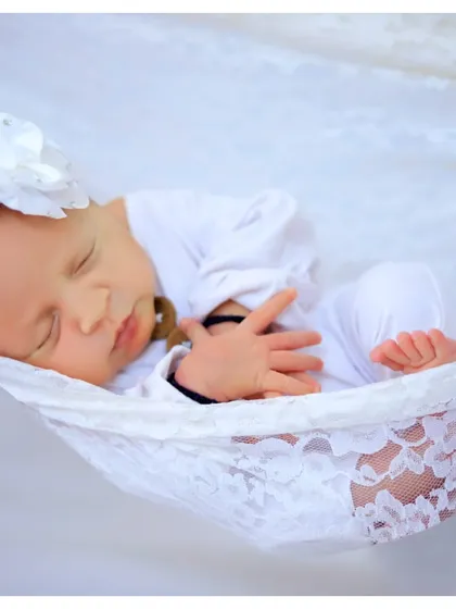 A peaceful newborn portrait capturing the baby's serene sleep in a delicate white lace hammock. This classic, minimalist setup focuses on the pure and gentle nature of your baby's first days.
