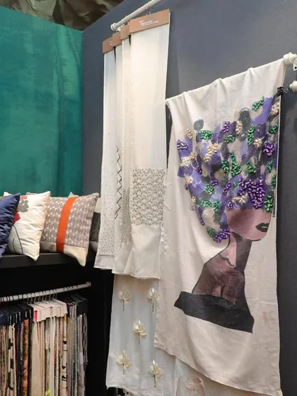 A display of our artisanal fabric and cushion creations. The centerpiece is a large fabric panel featuring a graphic portrait with 3D floral embellishments, alongside a variety of embroidered and patterned cushions, highlighting our most artistic and custom offerings.