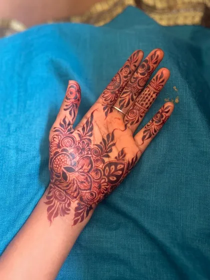 A beautiful and intricate party henna design covering the back of the hand. The pattern is a mix of floral and paisley motifs, perfect for any occasion.
