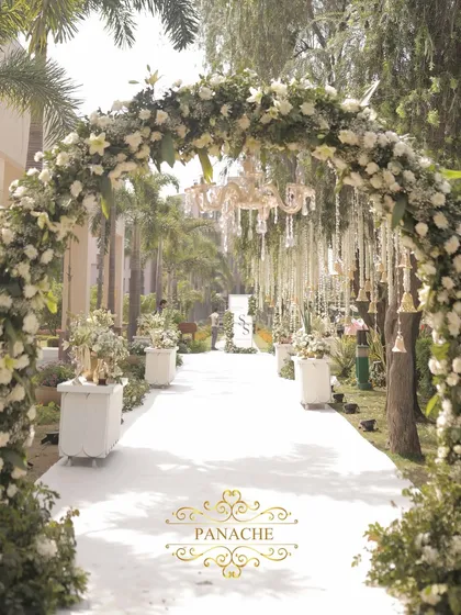 For this daytime wedding, we designed a heavenly aisle under a canopy of white floral arches and elegant chandeliers. It’s a testament to our love for creating serene, classic, and utterly romantic open-air ceremonies.