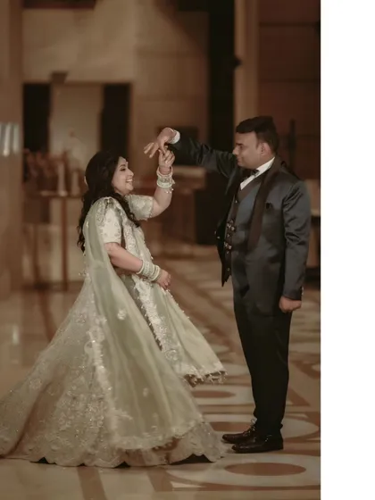 The couple shares a dance, his hand guiding her in a gentle twirl, capturing a moment of classic romance.