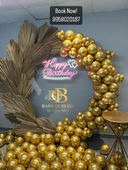 Pure glamour in gold. This stunning birthday backdrop features a full ring made of metallic gold balloons and dried golden palm leaves, with a neon sign at the center for a dazzling effect.