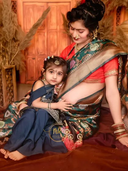 A tender moment between a mother and her older daughter. They are seated together, both dressed in beautiful traditional outfits, sharing a quiet moment of connection.