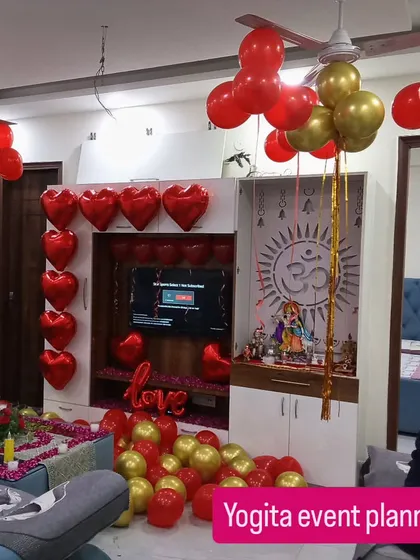 This is how I transform a living room for a surprise anniversary celebration. The decor includes red and gold balloons, heart-shaped balloons on the TV unit, and a beautifully decorated center table with flowers and candles.
