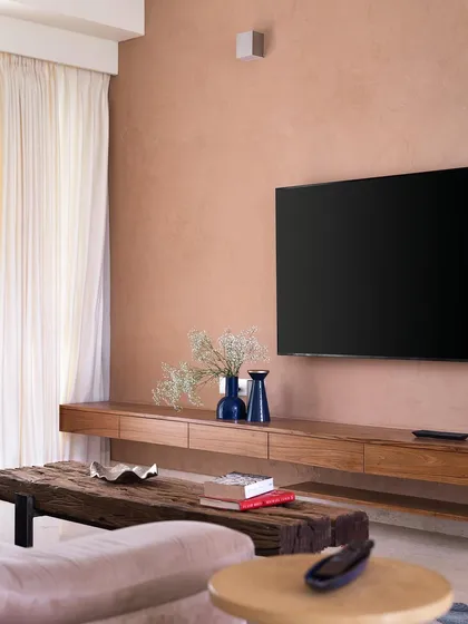 The family space in 'A Walk in the Clouds' features a floating wooden TV unit set against a peach-textured wall, complemented by a rustic sleeper wood coffee table.