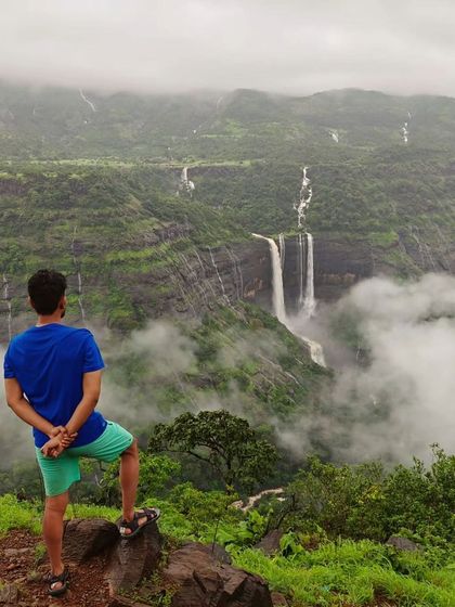 A stunning view of Kathaldar waterfalls in Maharashtra, with a trekker looking out at the multiple cascades through the mist.