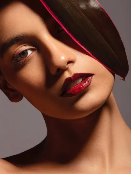 A minimalist yet powerful look, featuring a bold red lip and flawless skin, with a single leaf adding a touch of natural drama.