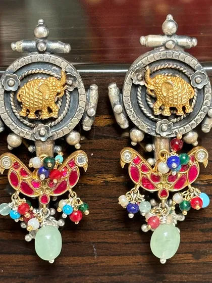 These fusion earrings feature a powerful elephant motif in gold plate set against an oxidised silver background. The colourful enamel work and dangling beads add a playful yet regal touch.