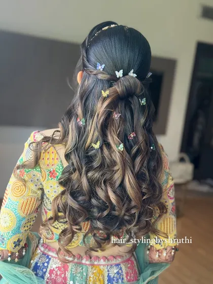 A playful and youthful half-up hairstyle with soft curls, decorated with whimsical multi-colored butterfly clips. This look is perfect for a vibrant Mehendi or Haldi ceremony.